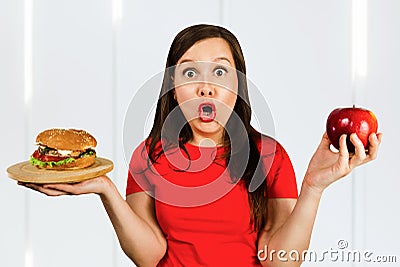 Portrait confused choice think woman holds burger and red apple and surprised Stock Photo