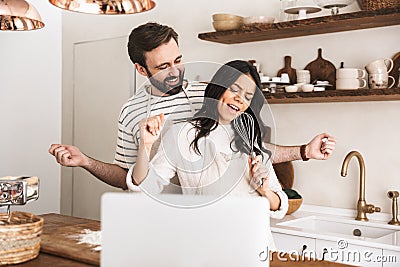 Portrait of content couple looking at laptop while cooking pastry in kitchen at home Stock Photo
