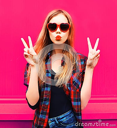 Portrait cool girl in heart shaped sunglasses sending sweet air kiss on colorful pink Stock Photo