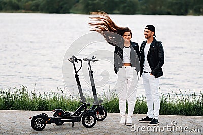 Portrait of a couple sitting near electric scooters, enjoying time in nature together, Two lovers on electric scooters.People on Stock Photo