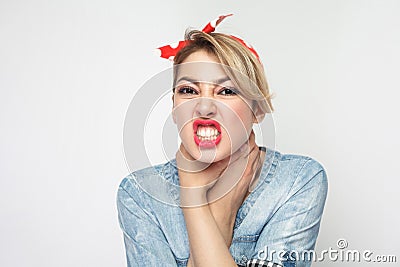 Portrait of crazy angry young woman in casual blue denim shirt with makeup and red headband standing, choke sheself and clenching Stock Photo