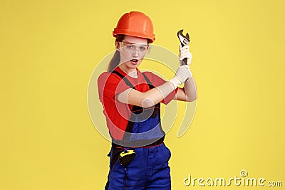 Crazy builder woman holding adjustable wrench, looking at camera with excited facial expression. Stock Photo