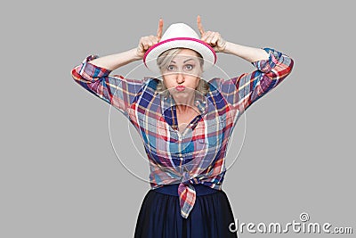 Portrait of crazy comic modern stylish mature woman in casual style with white hat standing with cow horns on head with hands and Stock Photo