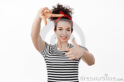 Portrait of creative young woman in headband, picturing moment, looking through hand frames gesture and smiling Stock Photo