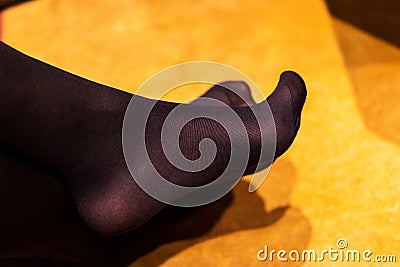 A portrait of the crossed feet of a girl wearing black opaque nylon pantyhose or stockings with a reinforced toe while sitting in Stock Photo