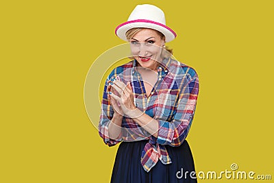 Portrait of cunning modern stylish mature woman in casual style with hat and eyeglasses standing in cunning gesture and looking at Stock Photo