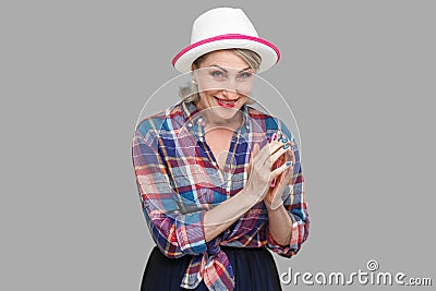 Portrait of cunning modern stylish mature woman in casual style with hat and eyeglasses standing in cunning gesture and looking at Stock Photo