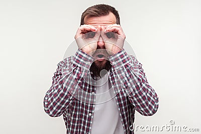 Portrait of curious wondered bearded man looking through fingers gesturing binoculars. white background Stock Photo