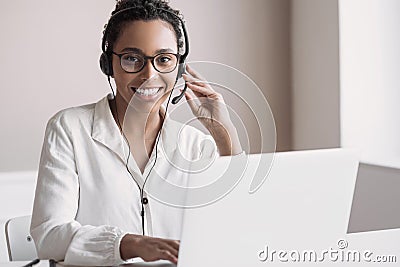 Portrait of customer service assistant talking on phone. Woman wearing headset working on laptop computer. Stock Photo