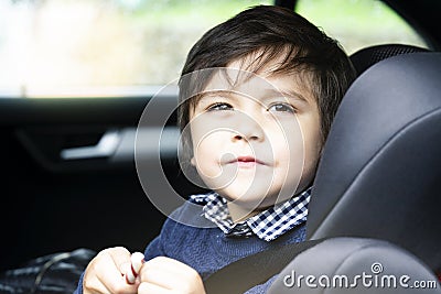 Portrait cut lilttle boy sitting in a car in safety chair, Adorable toddler boy sitting in car seat, Child in car seat with belt o Stock Photo