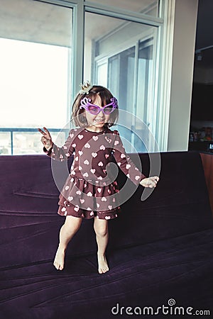 girl with funny glasses jumping dancing on couch indoors Stock Photo