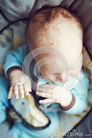 Portrait of cute adorable white Caucasian sleeping little baby boy newborn in blue clothes sitting in swing chair Stock Photo