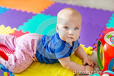 Portrait of cute baby boy lying on floor covered with multicolored soft mats in playroom. Adorable toddler kid smiling and playing Stock Photo