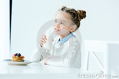 portrait of cute child with glass of milk in hand and homemade pancakes with honey and berries Stock Photo