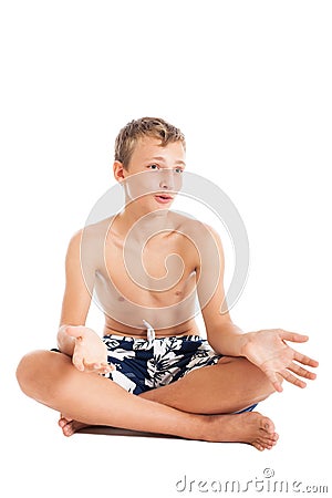 Portrait of a cute european teen boy wearing swimming shorts. A boy sitting on the floor. Stock Photo