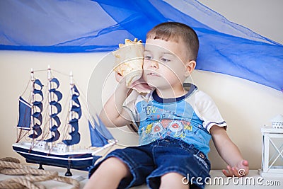Portrait of Cute and happy caucasian little boy carefully listening to a big cockleshell Stock Photo