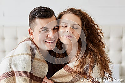 Portrait of cute happy couple sitting in bed embrace each other. Beautiful girl with long curly hair sits with closed eyes with Stock Photo