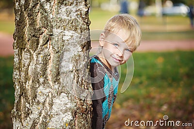 Portrait Cute little boy in a knitted sweater is playing behind a tree in autumn park, play at hide-and-seek Stock Photo