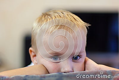 The portrait of cute little caucasian boy with light golden hair and blue eyes, with melancholy impression, propping up his head. Stock Photo