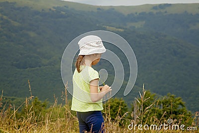 Portrait of cute little child girl in the grass against mountain background. Happy child have a rest in mountains Stock Photo