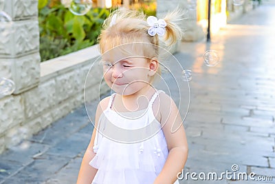 Portrait of cute little emotional blondy toddler girl in dress with soap bubbles breaking of her nose. Walk in the city park. Acti Stock Photo