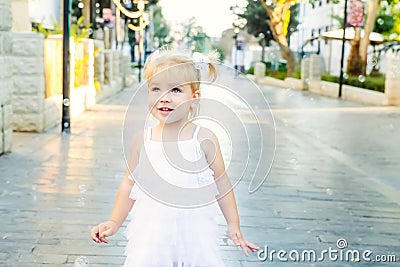 Portrait of cute little emotional blondy toddler girl in white dress playing and catching soap bubbles during walk in the city par Stock Photo