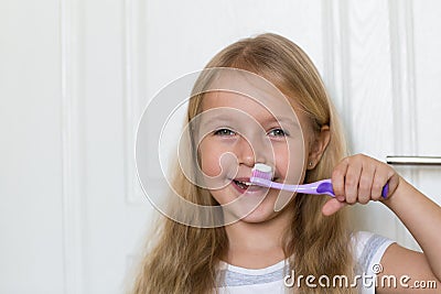 Portrait of cute little girl with blonde hair which cleaning tooth with brush and toothpaste in bathroom Stock Photo