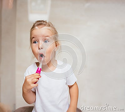 Portrait of cute little girl with blonde hair which cleaning tooth with brush and toothpaste in bathroom. Copyspace Stock Photo