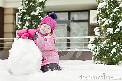 Portrait of cute little girl making smowman. at bright winter day. Adorable child playing with snow outdoors. Funny Stock Photo