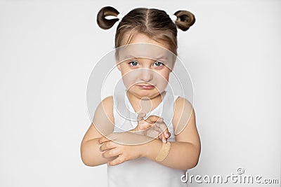 Portrait of cute pretty crying child girl, feeling pain because of wound on her arm, applying adhesive plaster bandage Stock Photo