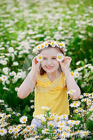 Portrait of a cute village girl in a wreath of daisies in a meadow. He holds a flower in his hands in front of his face. A child Stock Photo