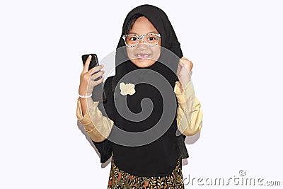 Portrait of cute A young asian little girl 6-7 years old muslim, wearing hijab, show face expression using a smart phone or Stock Photo