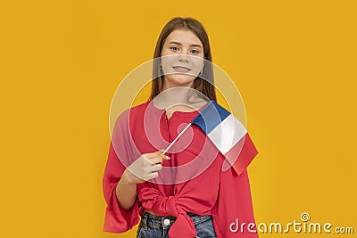 Portrait of cute young girl with the flag of France in her hands on orange background. Learn French. Immigration to France Stock Photo