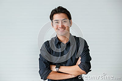 Portrait of a cute young and handsome Asian man in casual shirt fold his arms with confidence and pose to camera with warm smile Stock Photo