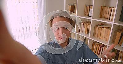 Portrait de clôture d'un jeune et beau blogueur caucasien en streaming dans la bibliothèque à l'intérieur banque de vidéos Portrait de clôture d'un jeune et beau blogueur caucasien en streaming dans la bibliothèque à l'intérieur banque de vidéos