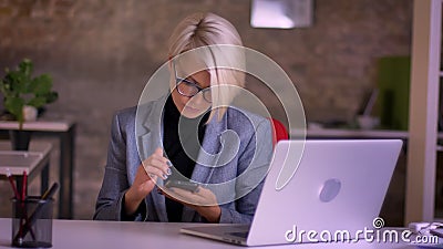 Portrait de femme d'affaires aux cheveux courts d'une cinquantaine d'années dans le fonctionnement en verre avec le smartphone de banque de vidéos Portrait de femme d'affaires aux cheveux courts d'une cinquantaine d'années dans le fonctionnement en verre avec le smartphone de banque de vidéos