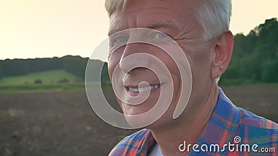 Portrait de vieil agriculteur regardant l'appareil-photo et le champ de sourire et cultivé pendant le matin à l'arrière-plan, heu banque de vidéos Portrait de vieil agriculteur regardant l'appareil-photo et le champ de sourire et cultivé pendant le matin à l'arrière-plan, heu banque de vidéos