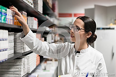 Dedicated pharmacist taking a medicine from the shelf during work Stock Photo