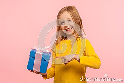 Portrait of delighted happy cute little girl pointing at gift box, boasting birthday present and smiling joyfully Stock Photo