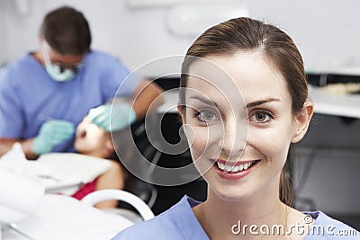 Portrait Of Dental Nurse With Dentist Examining Patient In Background Stock Photo