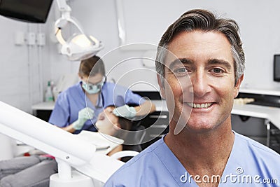 Portrait Of Dental Nurse With Dentist Examining Patient In Background Stock Photo