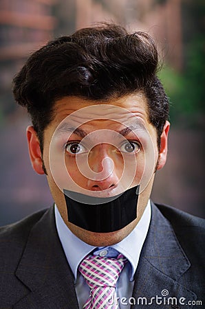 Portrait of a desperate businessman, with a black tape in his mouth, in a blurred background Stock Photo