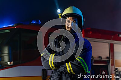 Portrait of dirty firefighter man on duty with fire truck in background at night, smiling. Stock Photo