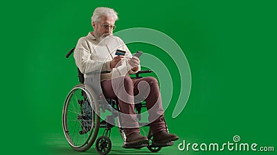 Portrait of disabled man isolated on chroma key green screen full shot. Senior bearded man sitting in wheelchair holding Stock Photo