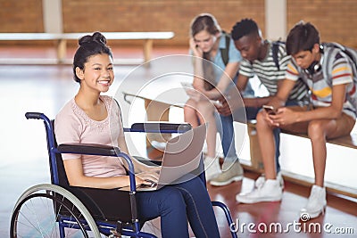 Portrait of disabled schoolgirl using laptop with classmates in background Stock Photo