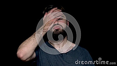 Portrait of disappointed, upset man with beard who covers his face with palm, isolated on black background. Disappointed Stock Photo