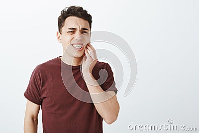 Portrait of displeased suffering young male model in red t-shirt, frowning and clenching fists, touching jaw while Stock Photo