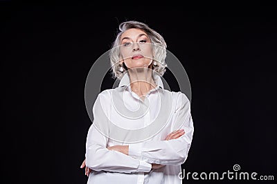 Portrait of a domineering, arrogant mature woman looking down and standing with her arms crossed isolated on a black Stock Photo