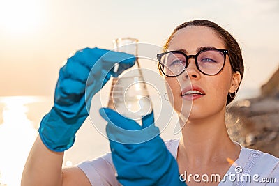 Portrait of ecologist wearing protective gloves and eyeglasses, examines test sample flask of water. Concept of Stock Photo