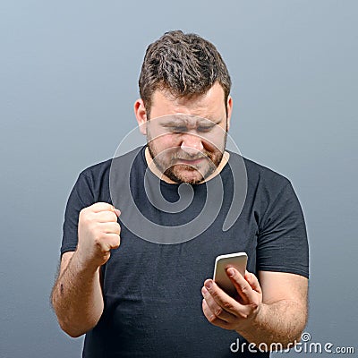 Portrait of ecstatic man holding cell phone and celebrating with closed fist against gray background Stock Photo